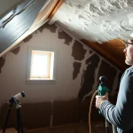 Spray foam causing damp identified by professionals as contractor inspects attic beams.